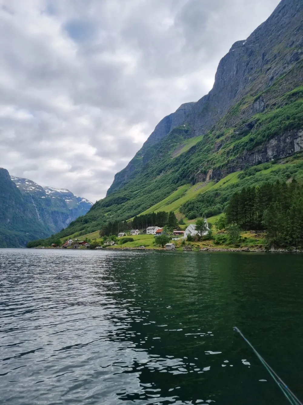Pieni kylä vuonon kallioseinämän juurella vedeltä nähtynä